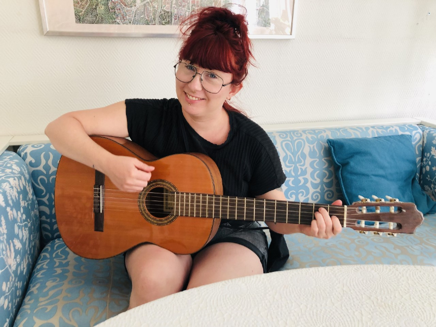 En kvinna i glasögon sitter i en soffa och håller i en gitarr.