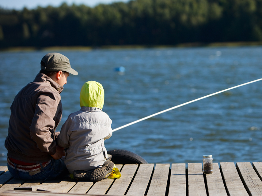 En man och ett barn sitter på en brygga och fiskar i en sjö. Foto: Mostphotos