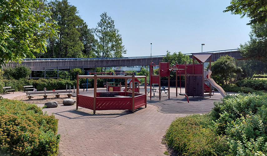 En lekplats med olika lekutrustning samt vid och solskydd i rött trä.