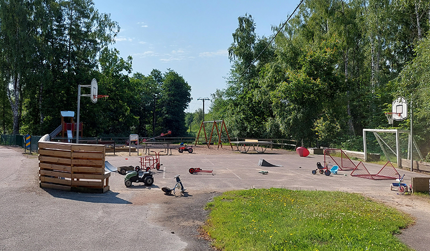 En lekplats med olika lekutrustning. Även pingisbord, basketkorg och fotbollsmål syns. Runt om på marken ligger olika leksaker utspridda.