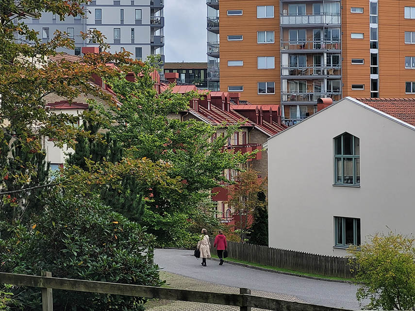 Två personer promenerar på en väg. Mölndals innerstad syns i bakgrunden. Man kan se både äldre och nyare byggnader