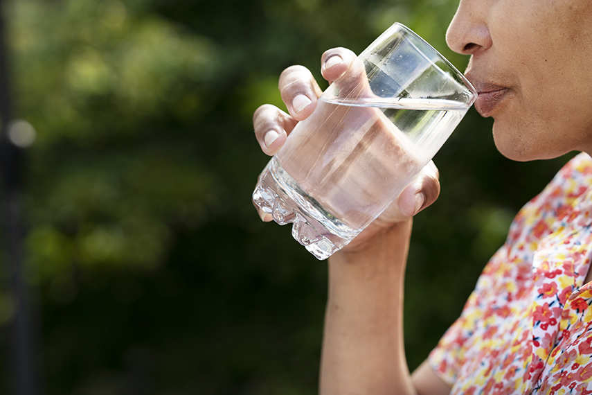 En person håller i ett vattenglas och för det mot sin mun.