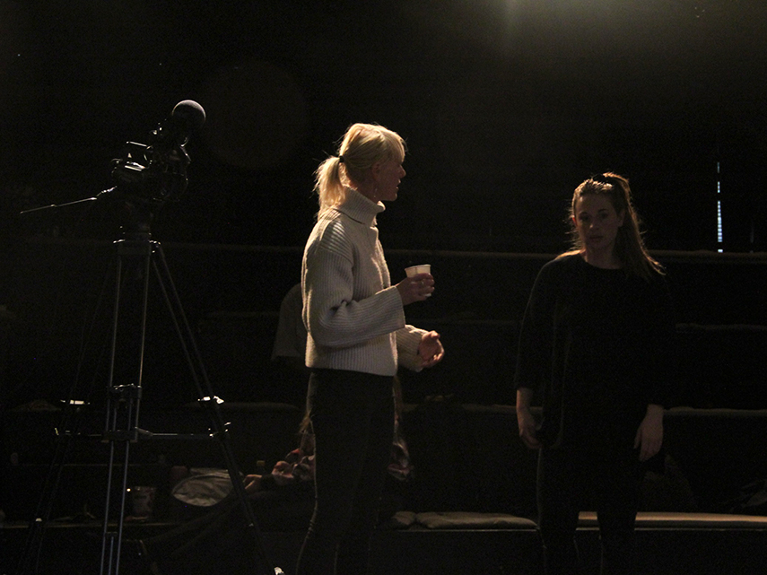 Två kvinnor står och pratar bredvid en filmkamera i ett mörkt rum