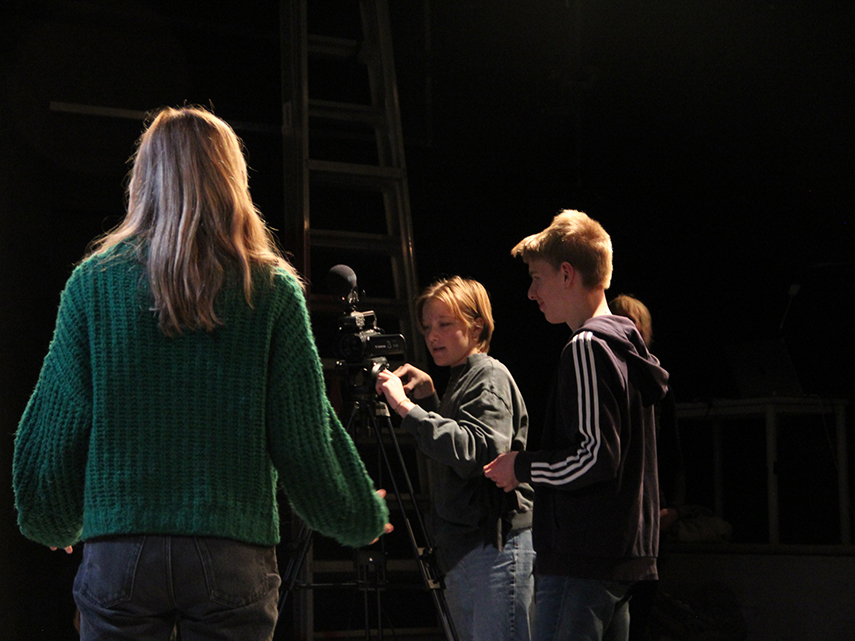 Tre ungdomar spelar in film med en filmkamera på stativ