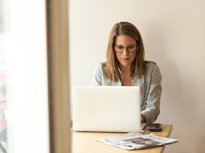En kvinna i glasögon sitter vid sin laptop.