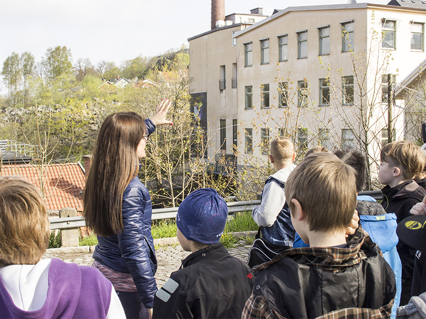 En grupp med barn tillsammans med museets pedagog ute i Kvarnbyn.