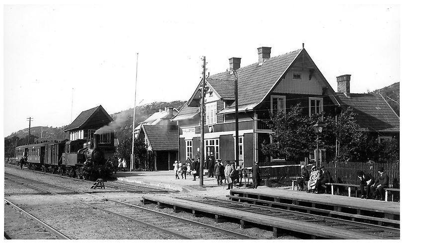 Vy över Kållereds stationshus, med tåg framför och personer på bänkar. Svartvitt. 1920-tal