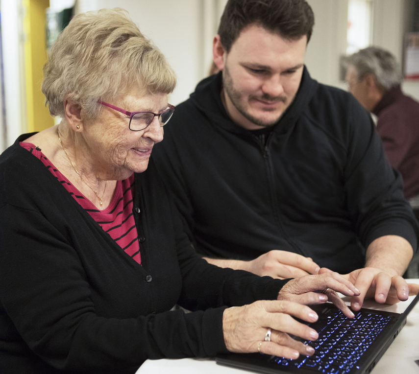 Äldre dam och yngre kille sitter och jobbar vid dator