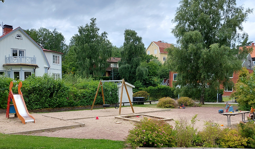 En lekplats med olika lekutrustning mitt i ett bostadsområde. 