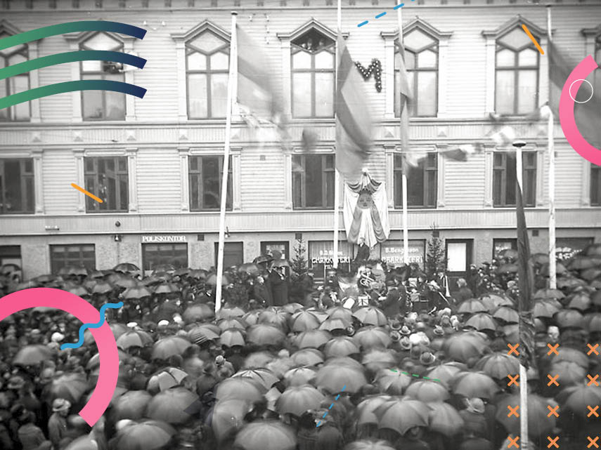Svartvit bild från stadsinvigningen i Mölndals, på nuvarande Gamla torget 1 januari 1922. Torget är fyllt med stor samling människor med sina paraplyer uppfällda. På fasaden och flaggstängerna är flaggor hissade.