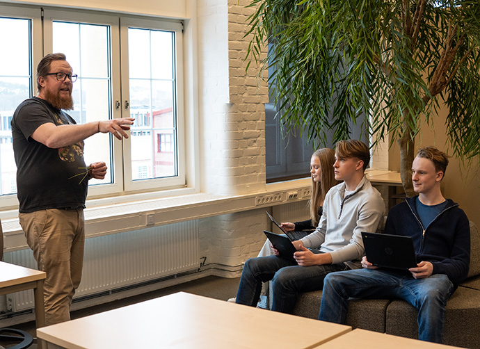 Lärare undervisar elevgrupp med laptops.