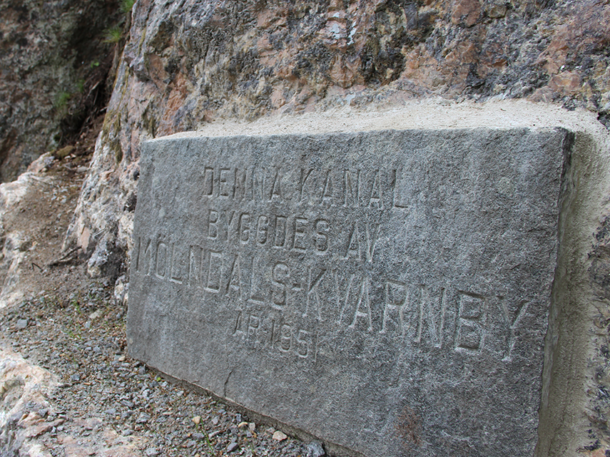 En minnessten sitter i en bergvägg med texten "Denna kanal byggdes av Mölndals Kvarnby 1851".