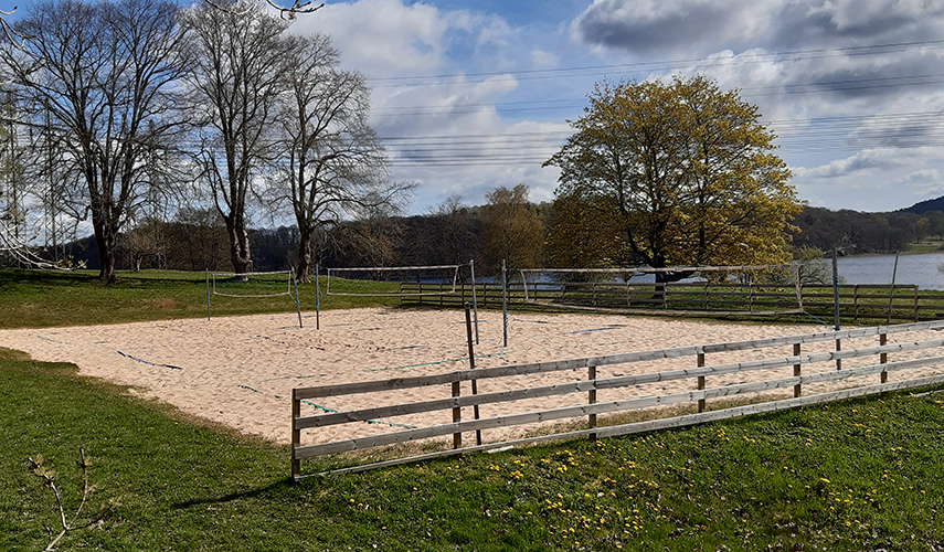 På en gräsmatta ligger sand i en stor kvadrat. tre stora volleybollnät är uppspända i sanden.