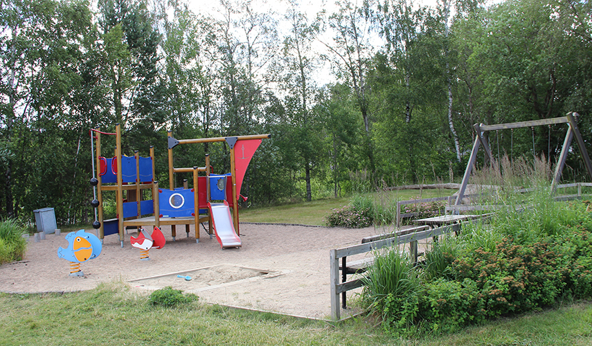 En lekplats med lekhus som ser ut som en båt, gungor och sandlåda.