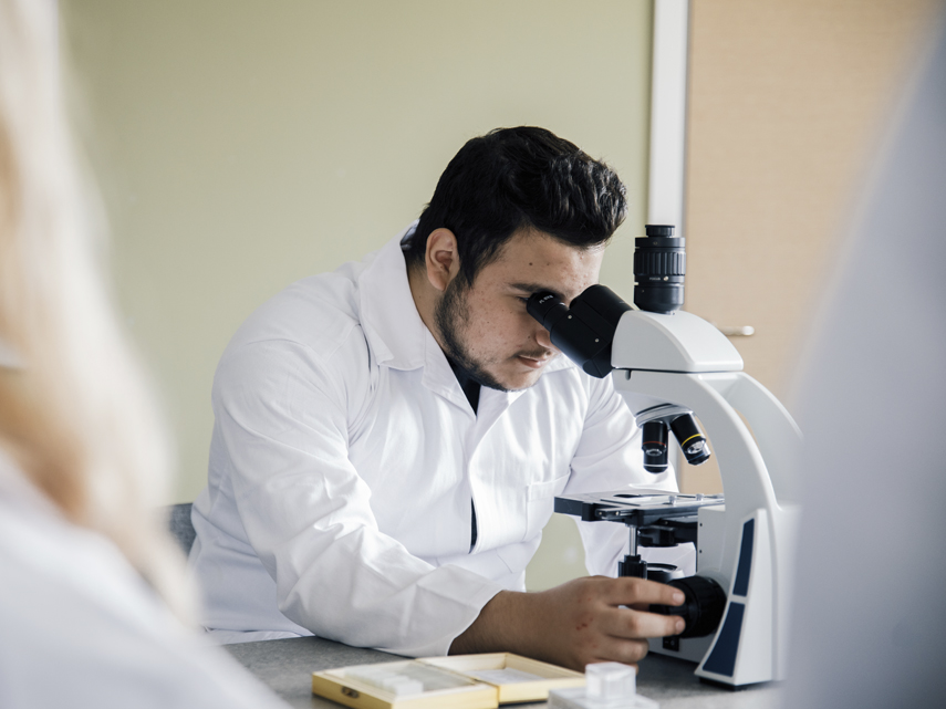 En manlig elev i vit rock tittar i ett mikroskop