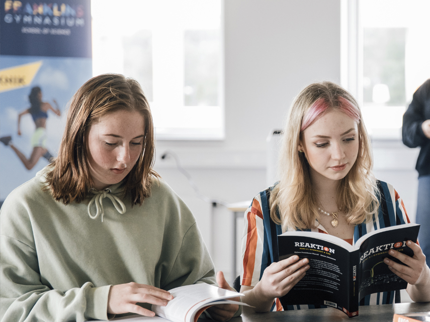 Två kvinnliga elever sitter tillsammans och studerar i några böcker