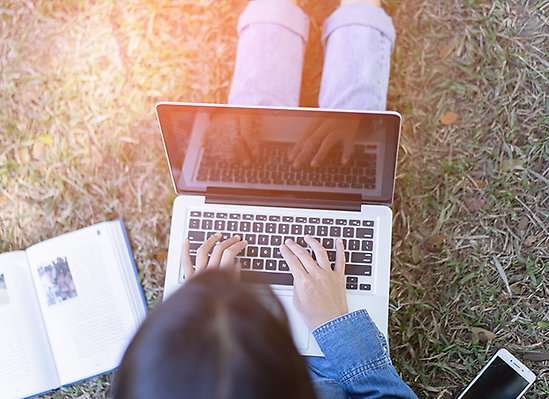 Person studerar med laptop utomhus på gräs.