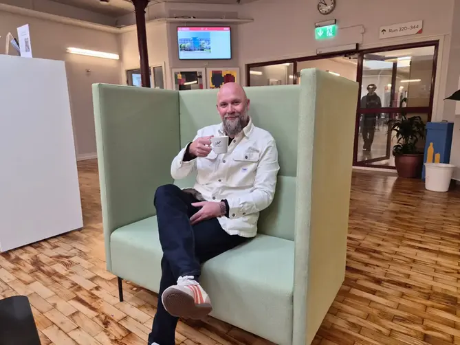Marcus sitter i en grön fåtölj med en kopp kaffe i handen