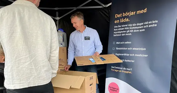 En man håller i en kartong framför en skylt med texten "Det börjar med en låda."