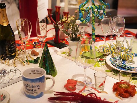 Ett dukat bord med högtidsprydnader. Champagneglas, midsommarstång, ljusstake, kräfthatt