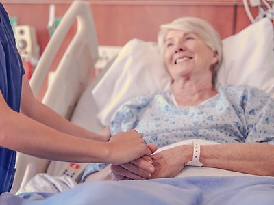 En undersköterska håller en patients hand.