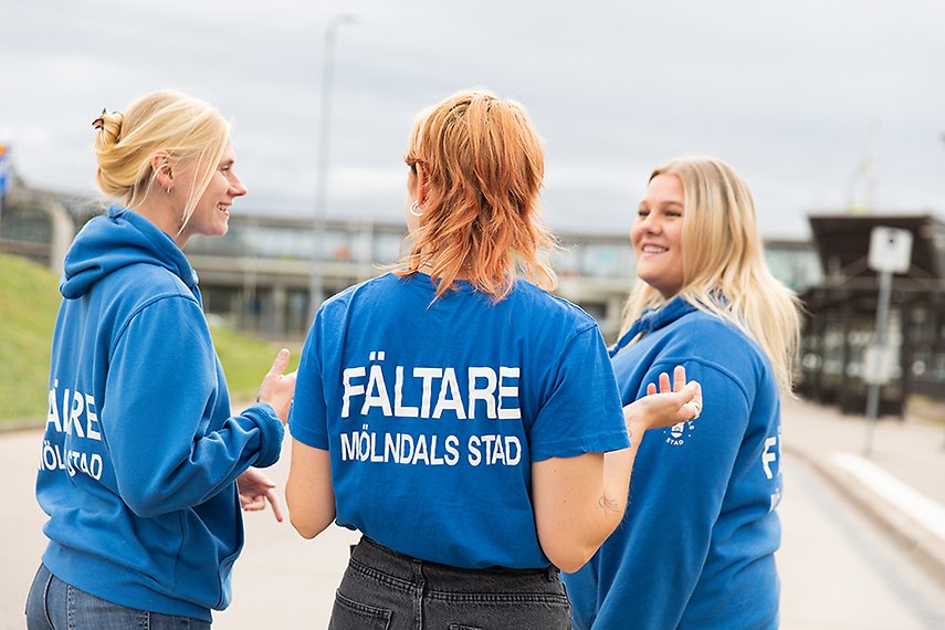 Tre fältare står vid Mölndals bro. Alla har blå tröjor på sig. En står med ryggen mot kameran. På ryggen står det "fältare Mölndals stad".