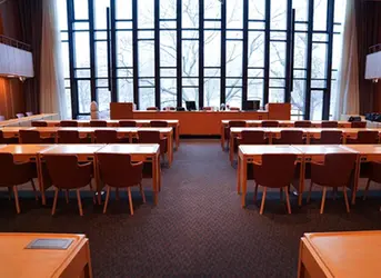 Mölndals fullmäktigesal, ett stort rum med flera rader av bord och stolar framför ett stort väggtäckande fönsterparti .