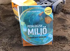 bok i sandlåda med gul leksakslastbil i bakgrunden