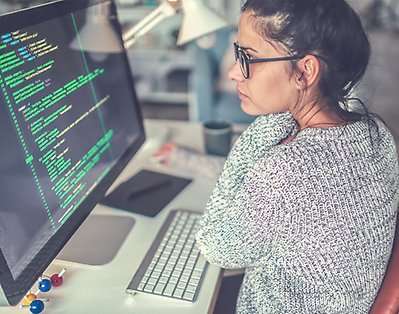 En kvinna sitter vid en laptop med kod på skärmen.