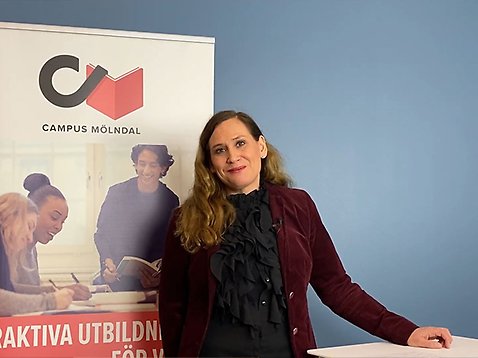 Chefen för Campus Mölndal ler mot kameran medan hon står framför en banner.