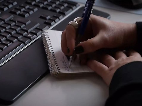 En hand syns hålla en penna och skriva på ett block.