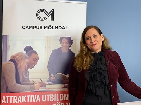 En kvinna ler mot kameran framför en rollup med Campus Mölndals logotyp.